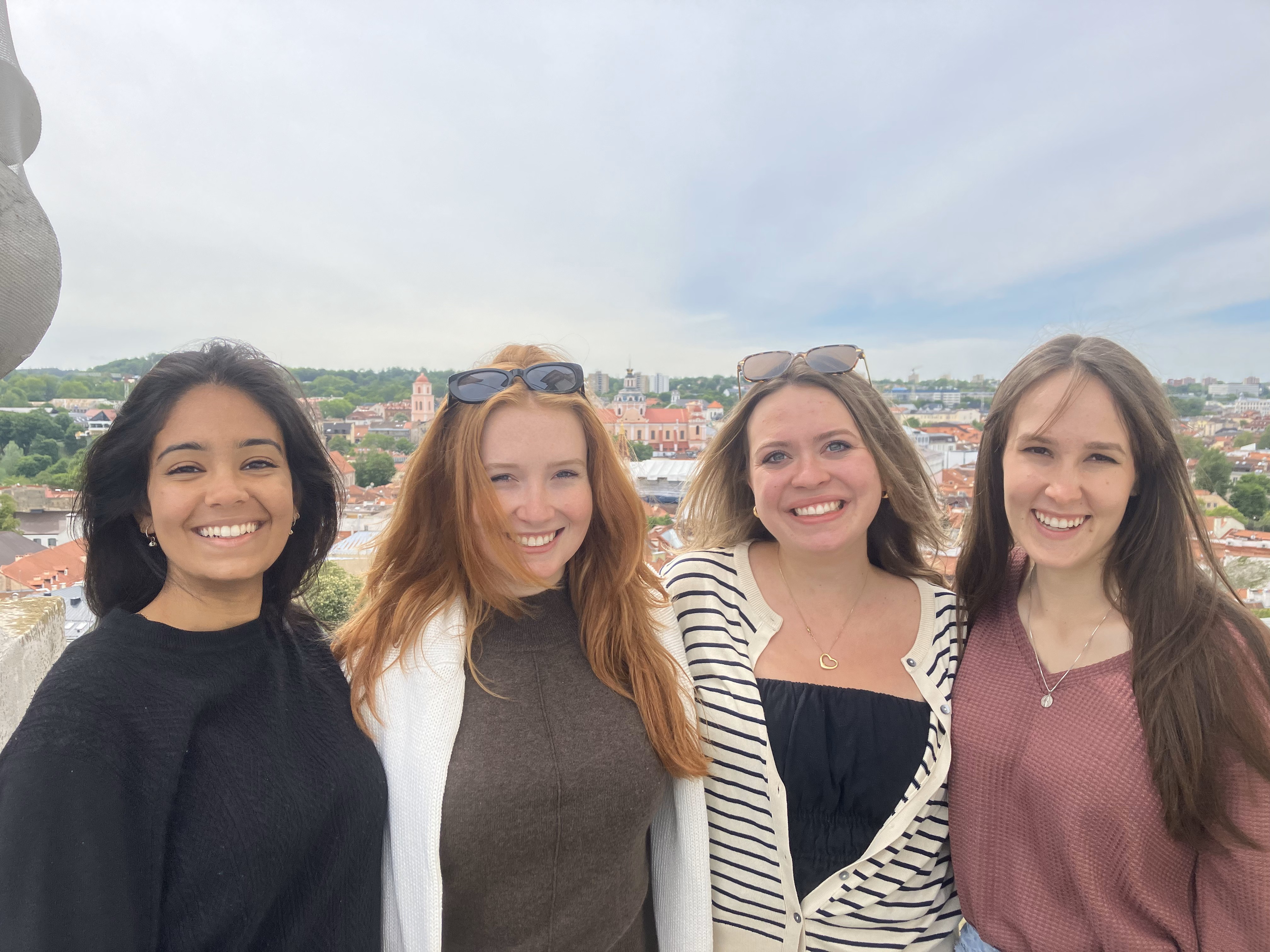 Four University Singer students posing for a photo with Lithuanian town in background