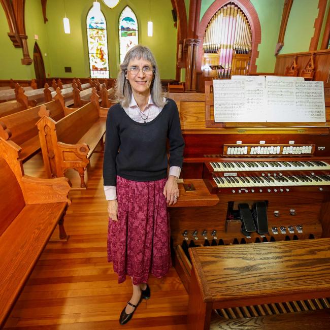 UVA Department of Music instructor Barbara Moore standing next to pipe organ keyboard console in the UVA Chapel.